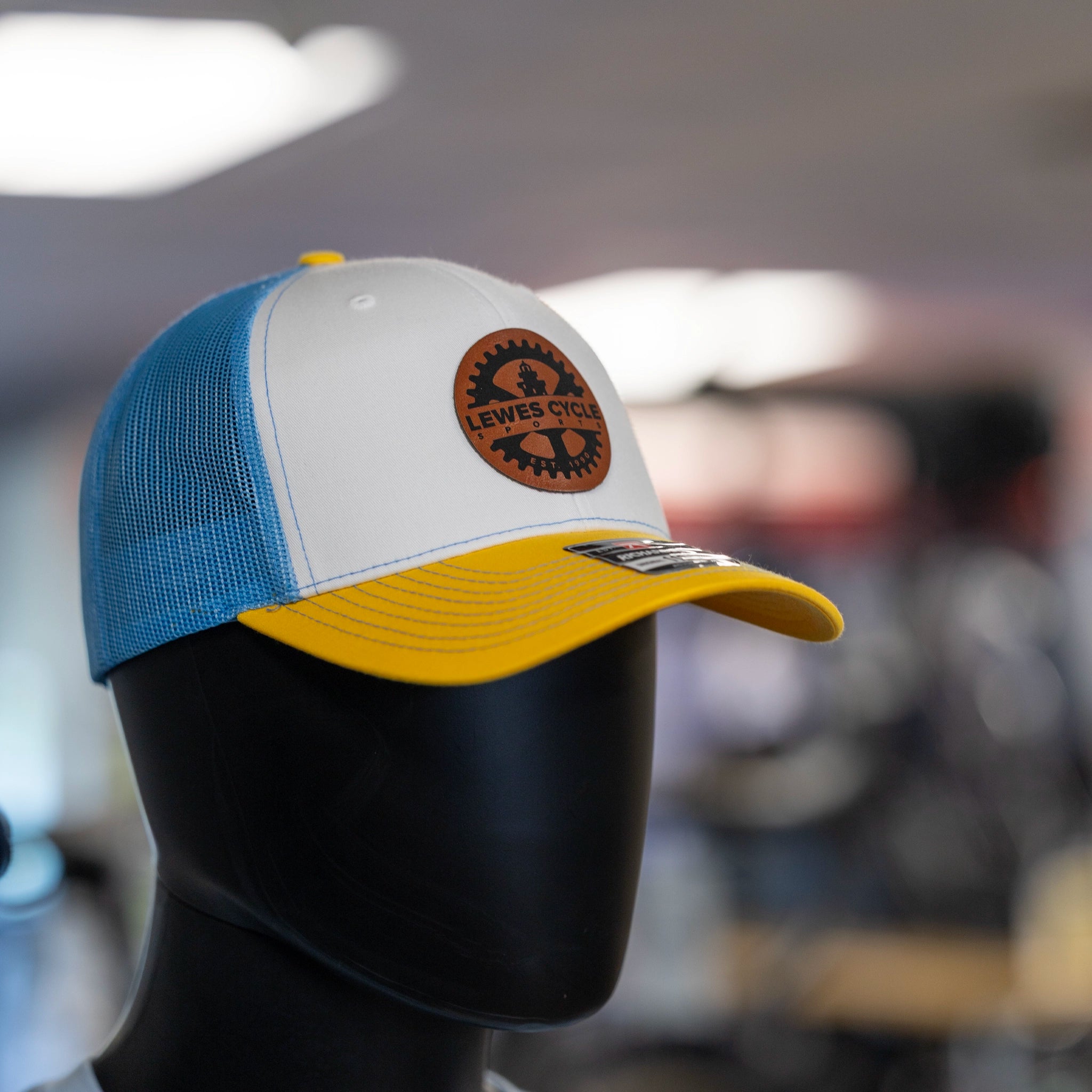 Lewes Cycle Sports yellow and blue trucker cap with leather patch logo front closeup view