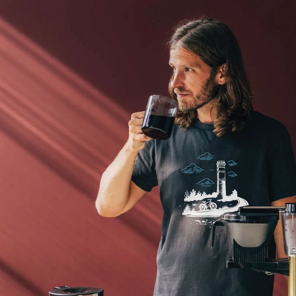 Man drinking coffee wearing Lewes Cycle Sports tower t-shirt with Fort Miles design