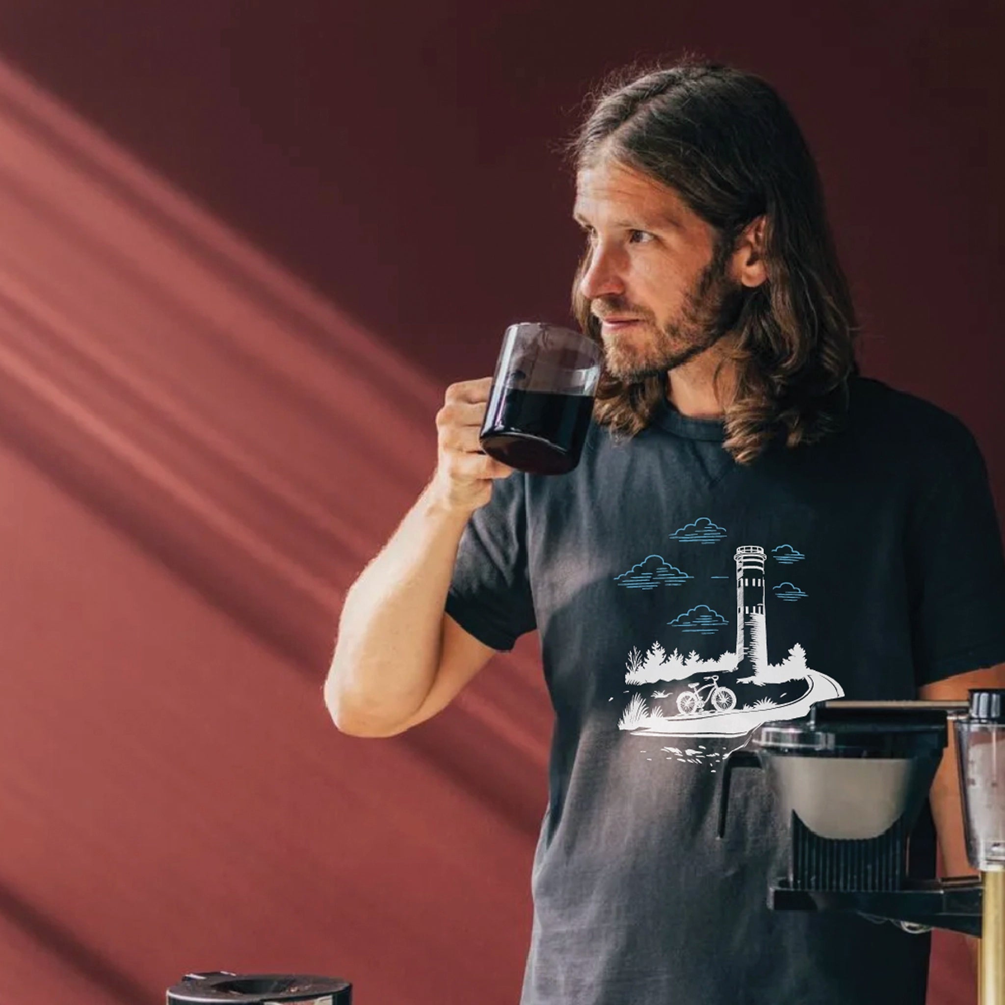 Man drinking coffee wearing Lewes Cycle Sports tower t-shirt with Fort Miles design